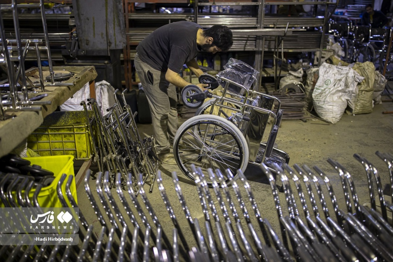 یکی از کارگران کم شنوا گارگاه ویلچر سازی مشغول نصب چرخ های کوچک ویلچر است
