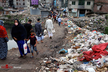مردم در امتداد جاده ای که در میان انبوهی از زباله ها قرار دارد قدم می زنند، داکا، بنگلادش.
