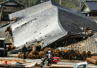 پست چی ژاپنی در کنار ساختمانی در وادزیمه که در اثر زلزله واژگون شده است

