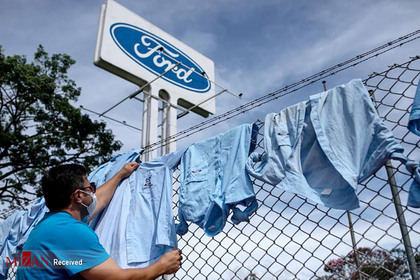 اعلام بسته شدن کاخانه فورد در برزیل برای سه ماه و کارگری که لباس هایش را پهن کرده است.